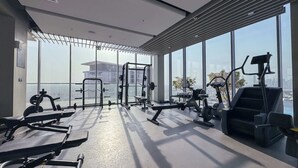 A modern gym with various exercise equipment, large windows, and a view of a cityscape.