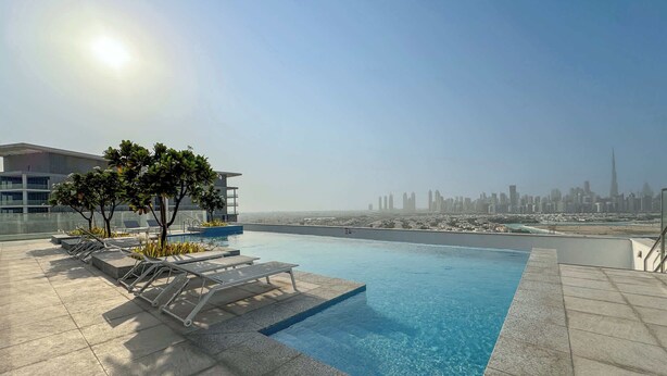 A rooftop pool with lounge chairs and a view of a city skyline.