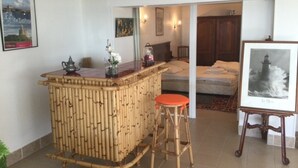 A room with a bamboo bar area, a bed, and a framed picture of a lighthouse. - 1-bedroom Apartment With View of Private Beach (Agon-Coutainville)