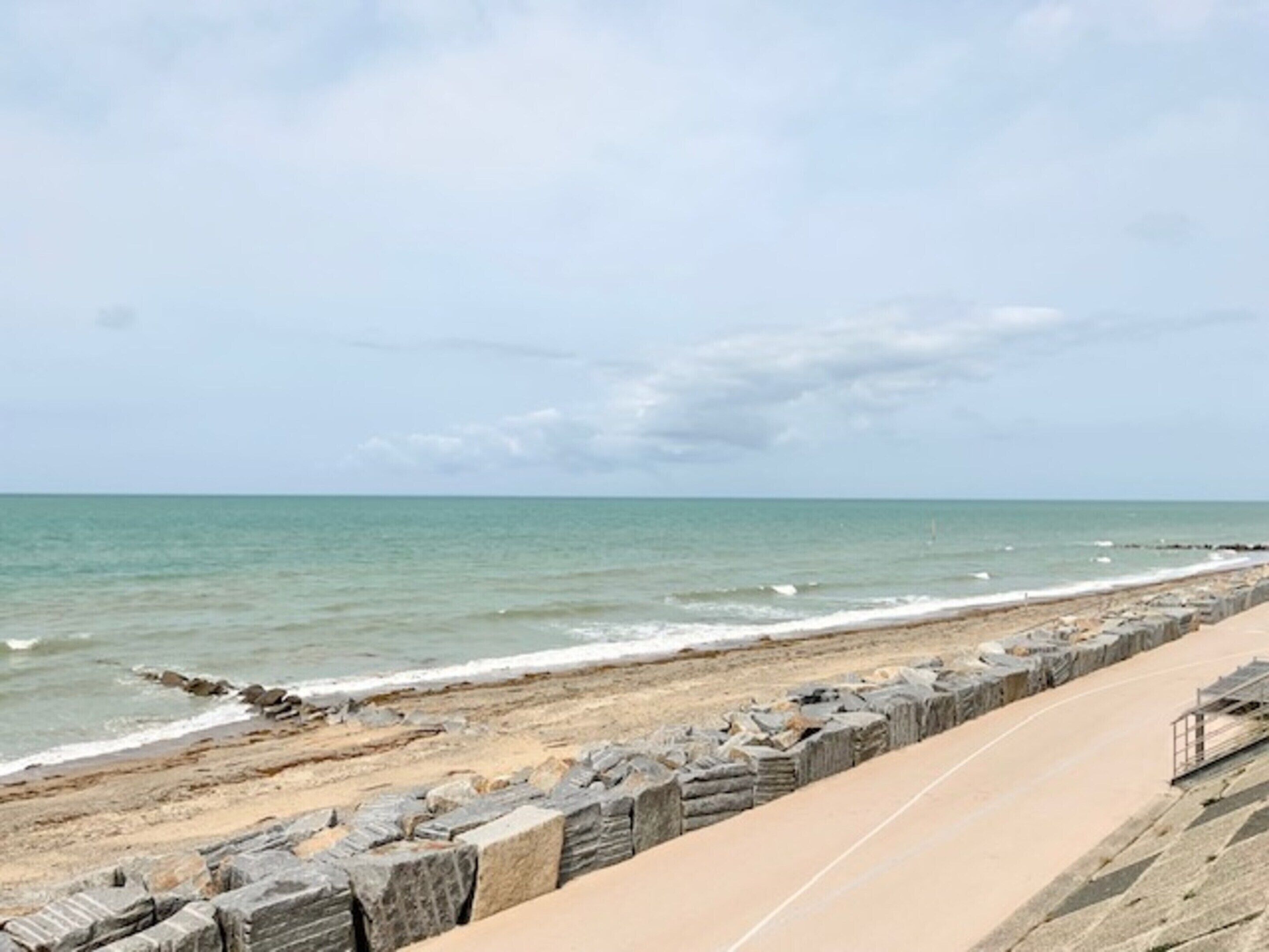 A beach with a concrete walkway and a rocky barrier.