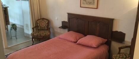 Une chambre à coucher avec un grand lit, une chaise, une table de chevet et une lampe fixée au mur.