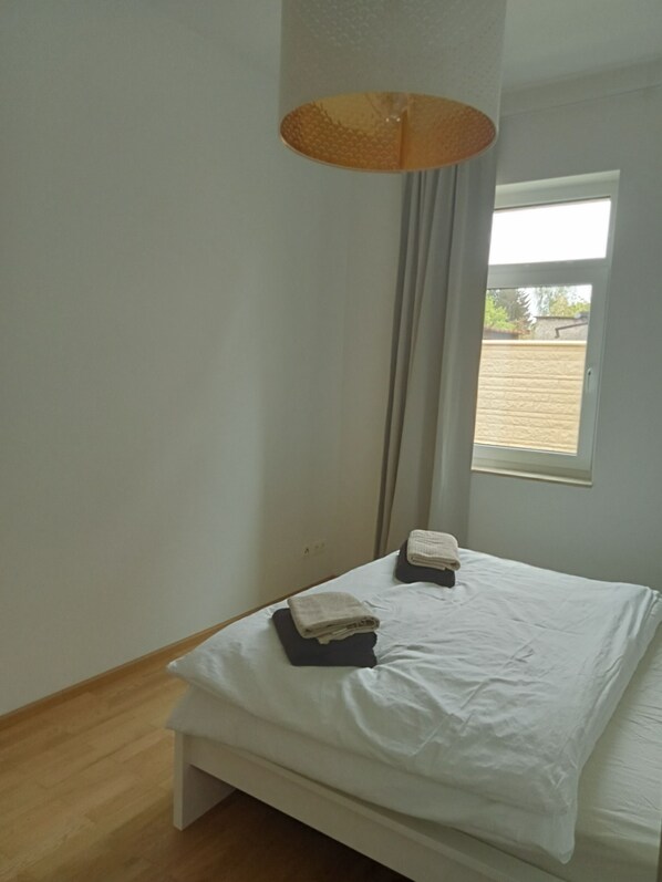 A bedroom with a bed, a window, and a hanging light fixture.
