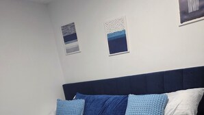 A neatly made bed with a blue quilt and pillows, a striped blanket, and a folded towel on the bed.