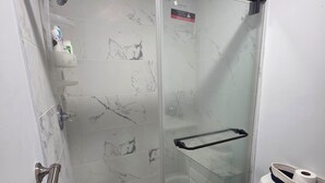 A bathroom with a glass-enclosed shower, a toilet, and a marble-tiled floor.