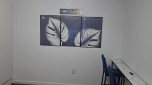 A room with a white ceiling, a 'WELCOME' sign, a wall-mounted artwork, a white table with a marble pattern, and blue chairs.