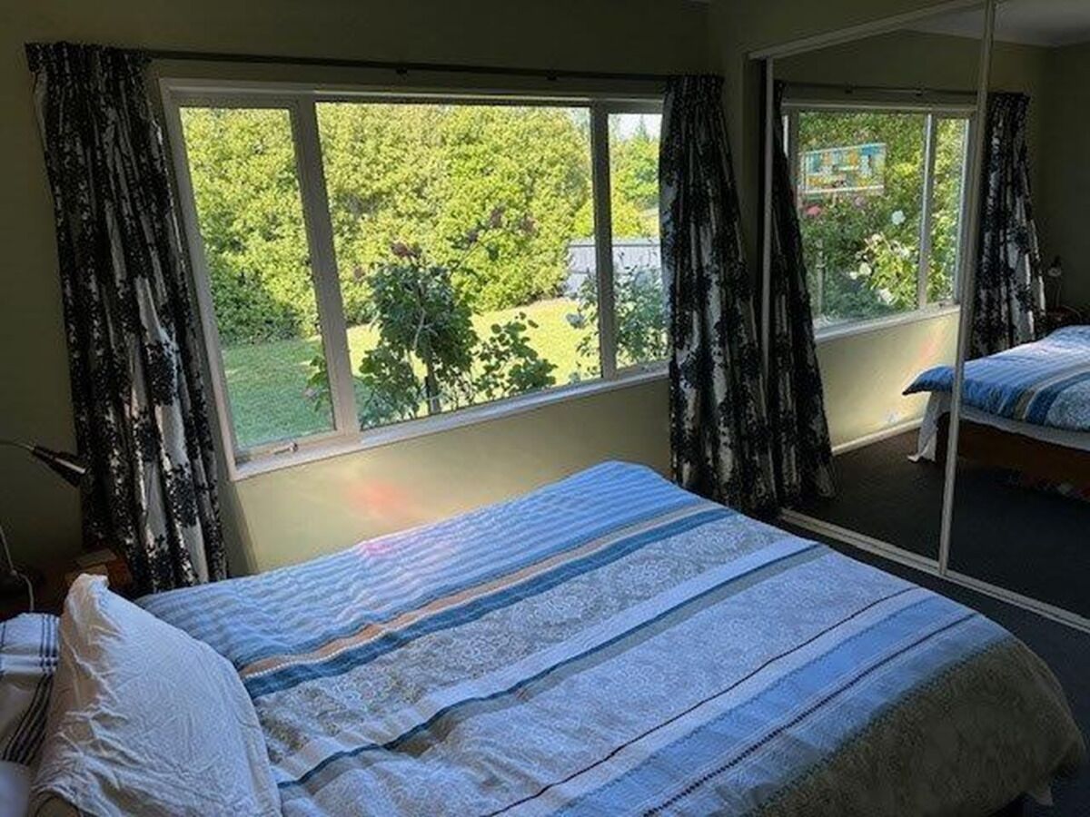 A bedroom with a large window, a bed with striped bedding, and a view of greenery outside.