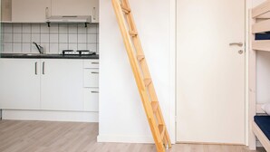 Et lille køkken med hvide skabe, en komfur og en træstige, der læner sig op ad en hvid dør.