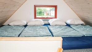 Et trekantet soveværelse på loftet med et vindue, to senge og en træloft.