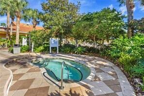 A swimming pool with a curved design, surrounded by a tiled walkway and lush greenery, including palm trees and various plants. - Bright 3B w Pool Close to Disney Encantada 8545 (Kissimmee)