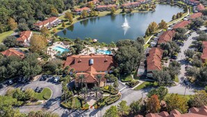 An aerial view of a residential area with a large lake, surrounded by houses with red roofs, a swimming pool, and a fountain. - Bright 3B w Pool Close to Disney Encantada 8545 (Kissimmee)