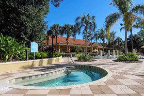 A pool area with a circular hot tub, palm trees, and a building with a red roof. - Bright 3B w Pool Close to Disney Encantada 8545 (Kissimmee)