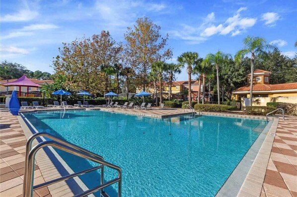 A swimming pool with lounge chairs and umbrellas, surrounded by palm trees and buildings. - Bright 3B w Pool Close to Disney Encantada 8545 (Kissimmee)