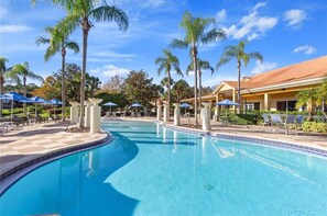 A swimming pool with lounge chairs and umbrellas, surrounded by palm trees and a building with a red roof. - Bright 3B w Pool Close to Disney Encantada 8545 (Kissimmee)