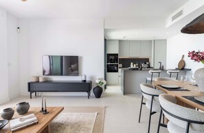 A modern living room with a flat-screen TV, a wooden coffee table, and a dining area with a wooden table and chairs. - Casa Lucia Mediterranean Garden Suite Higueron (Fuengirola)