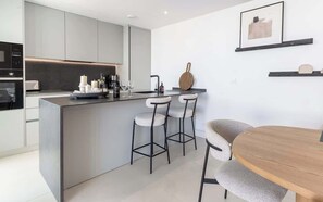 A modern kitchen with a central island, bar stools, and a dining table.