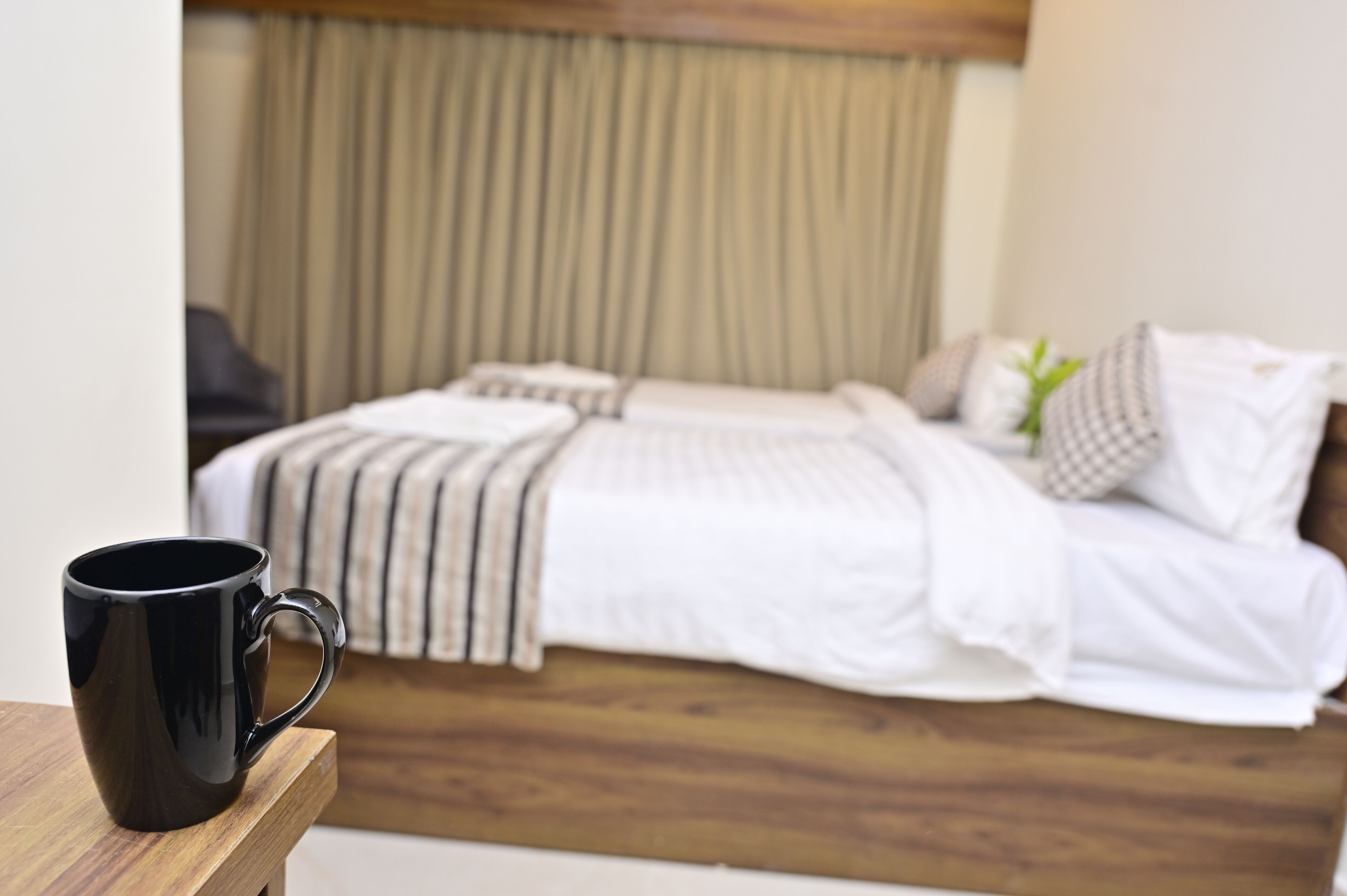 Un lit avec une tête de lit en bois, une couvre-lit blanche et une tasse noire posée sur une table en bois.