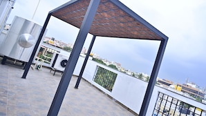 Eine Dachterrasse mit einer Metall-Pergola, Fitnessgeräten und Blick auf die Stadtlandschaft.