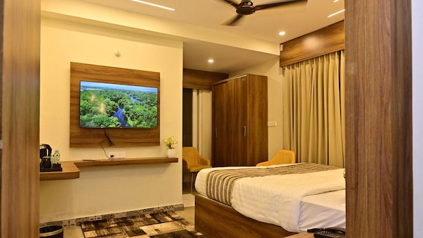 Ein modernes Hotelzimmer mit einem großen Bett, einem Holzschrank, einem Wand-Fernseher und einem Deckenventilator.