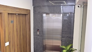 Ein moderner Aufzug mit Glastür, daneben eine Holztür und ein Blumentopf.