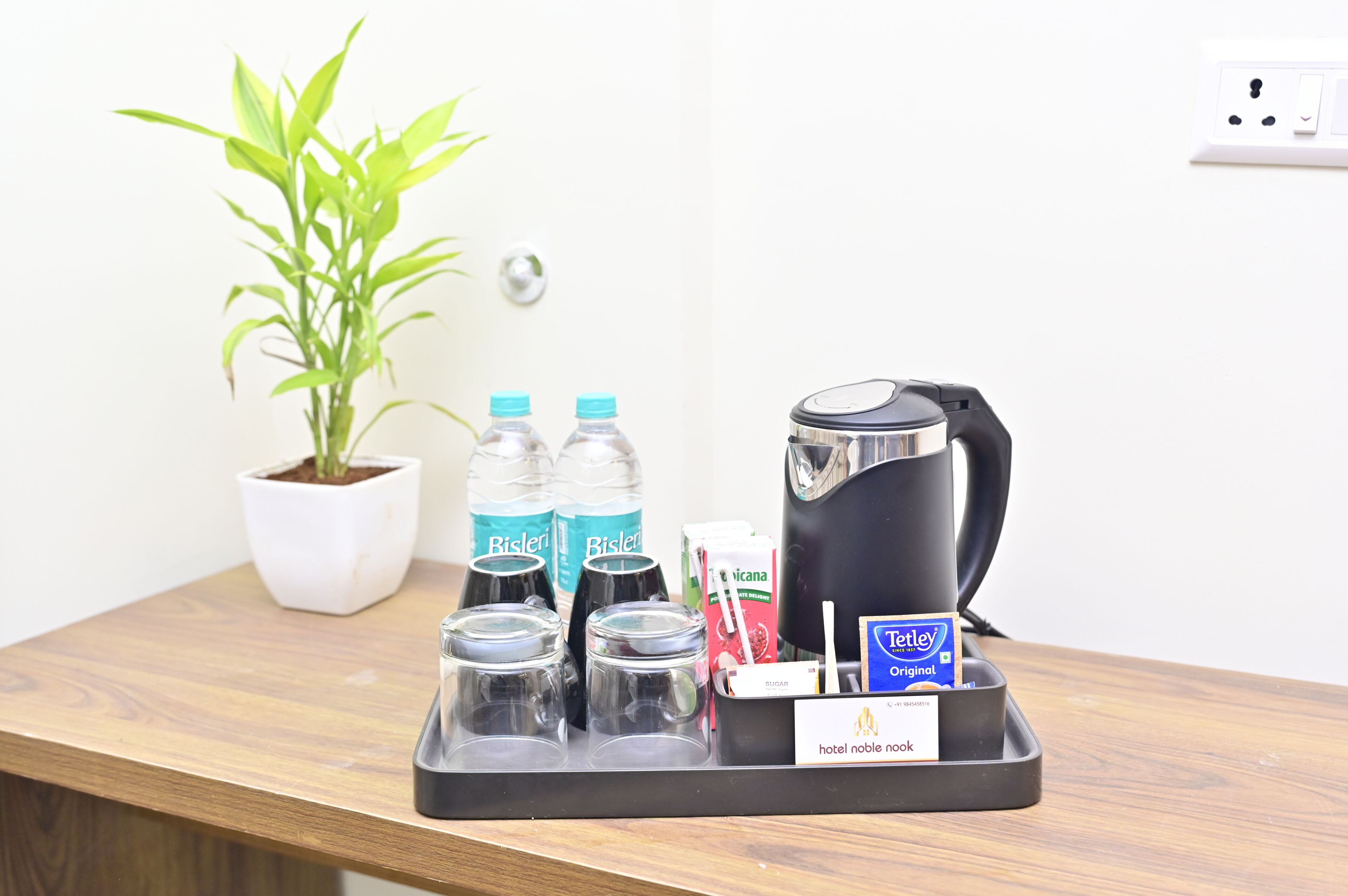 A hotel room's minibar with a coffee maker, Bisleri water bottles, a carton of milk, and a Tetley tea box.