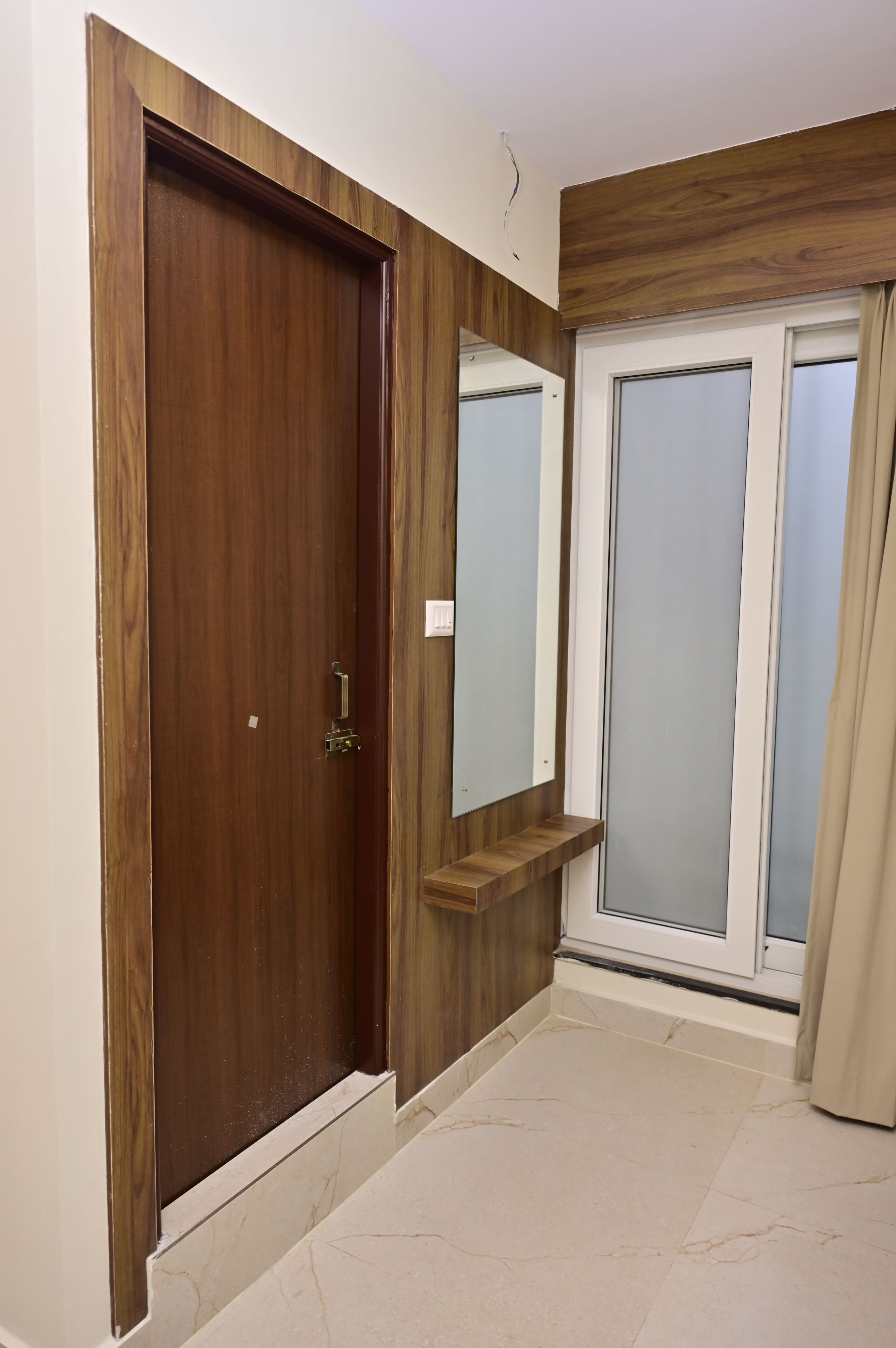 Un couloir avec une porte en bois, un miroir et une fenêtre avec des rideaux.
