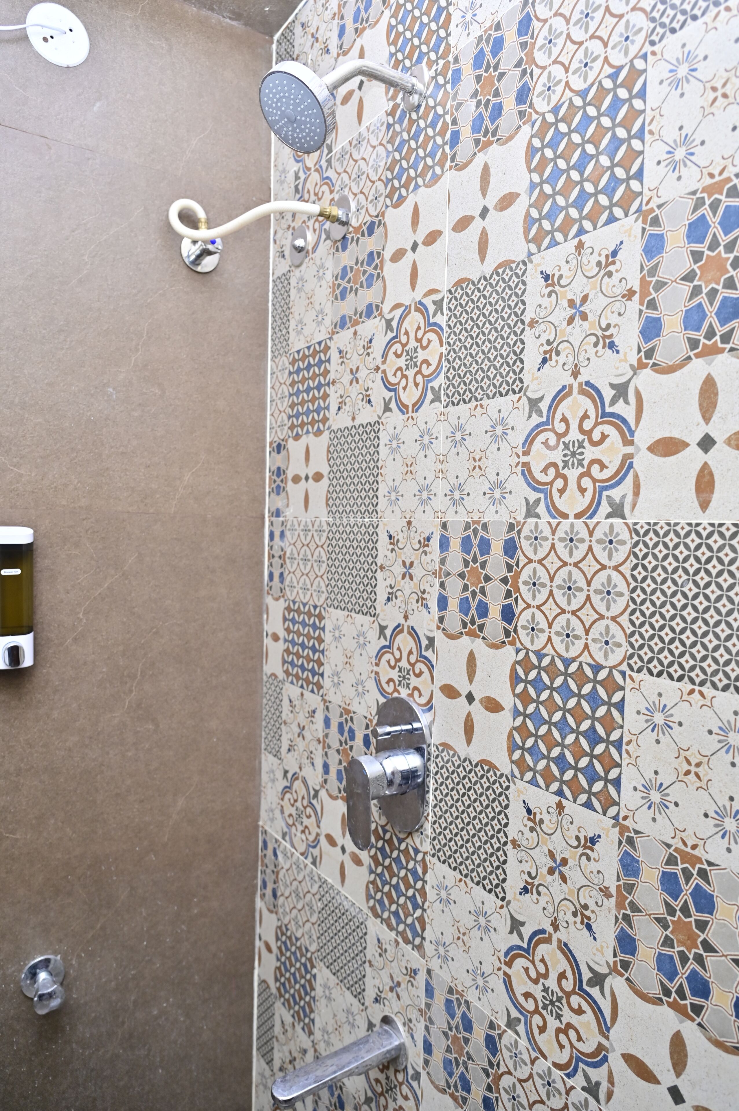 A shower with a handheld showerhead and a wall with a mosaic tile pattern.