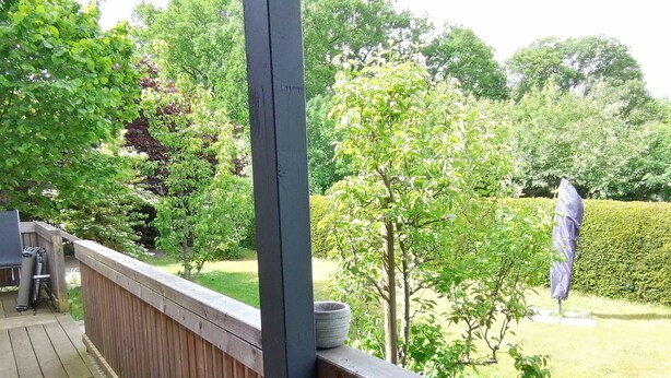 Une terrasse en bois avec une balustrade, une petite table sur laquelle se trouve un bol, et une statue en arrière-plan.