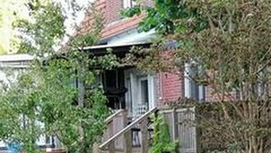 Une maison d’habitation avec un porche à l’avant, un petit jardin et un mur en briques.