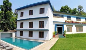 Ein zweistöckiges Gebäude mit Schwimmbad, gepflegtem Rasen und einem Balkon mit Topfpflanzen.