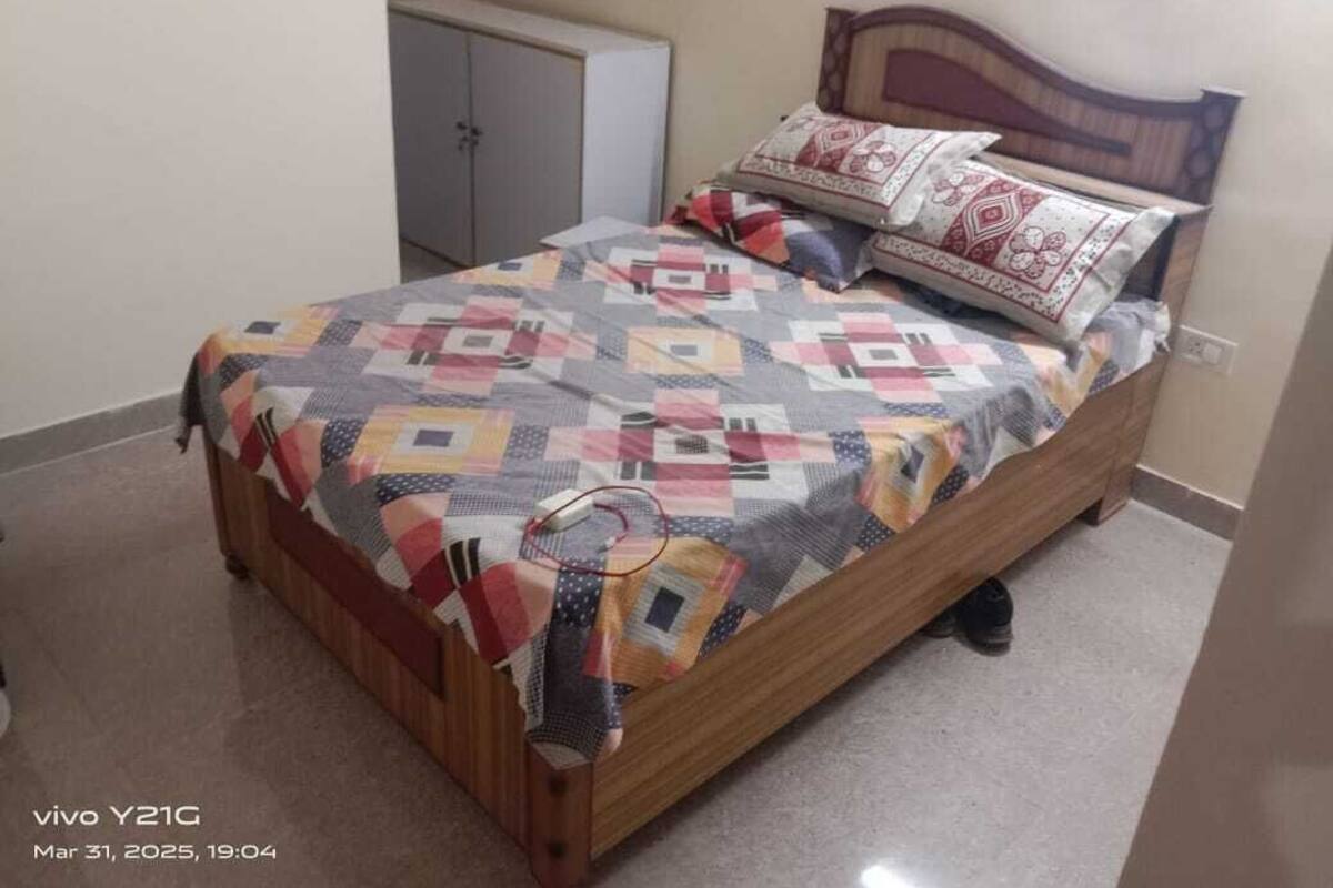A bed with a quilt, pillows, and a wooden headboard in a room with a cabinet.