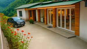Una casa moderna con un coche estacionado frente, rodeada de un jardín con flores rojas.