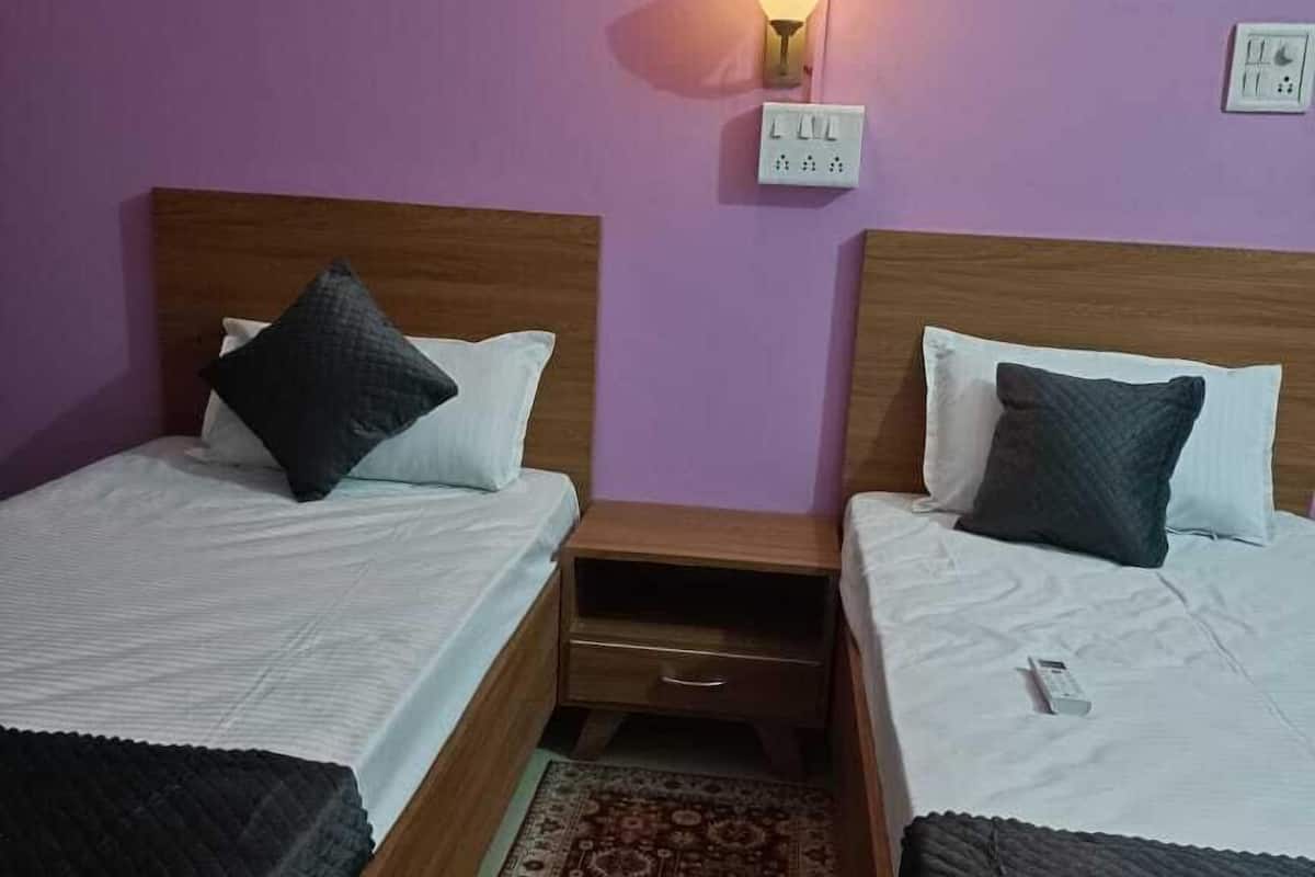 A room with two single beds, a nightstand between them, a wall socket, and a patterned rug.