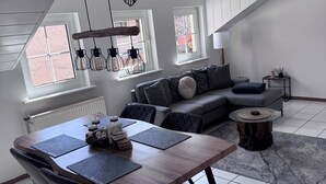 A modern living room with a dining table, grey sofa, and a decorative deer head on the wall.