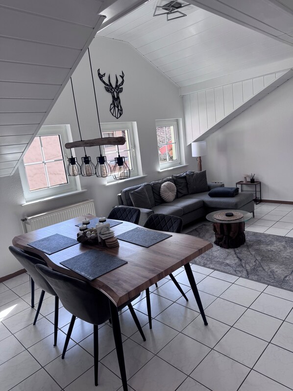 A modern living room with a dining table, grey sofa, and a decorative deer head on the wall.