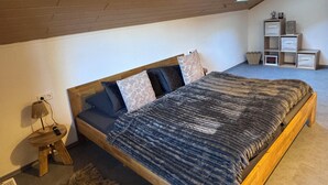 A bedroom with a wooden bed, a small bedside table, a lamp, a fur rug, and a storage unit against the wall.