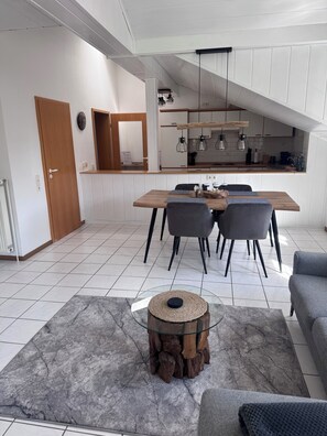 A modern kitchen with white cabinets, a wooden dining table, and a built-in oven.