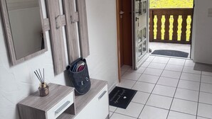 A room with a wooden cabinet, a mirror, a welcome bag, and a door leading to a balcony with a view of greenery.