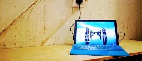A laptop on a wooden table with a visible power outlet in the background.