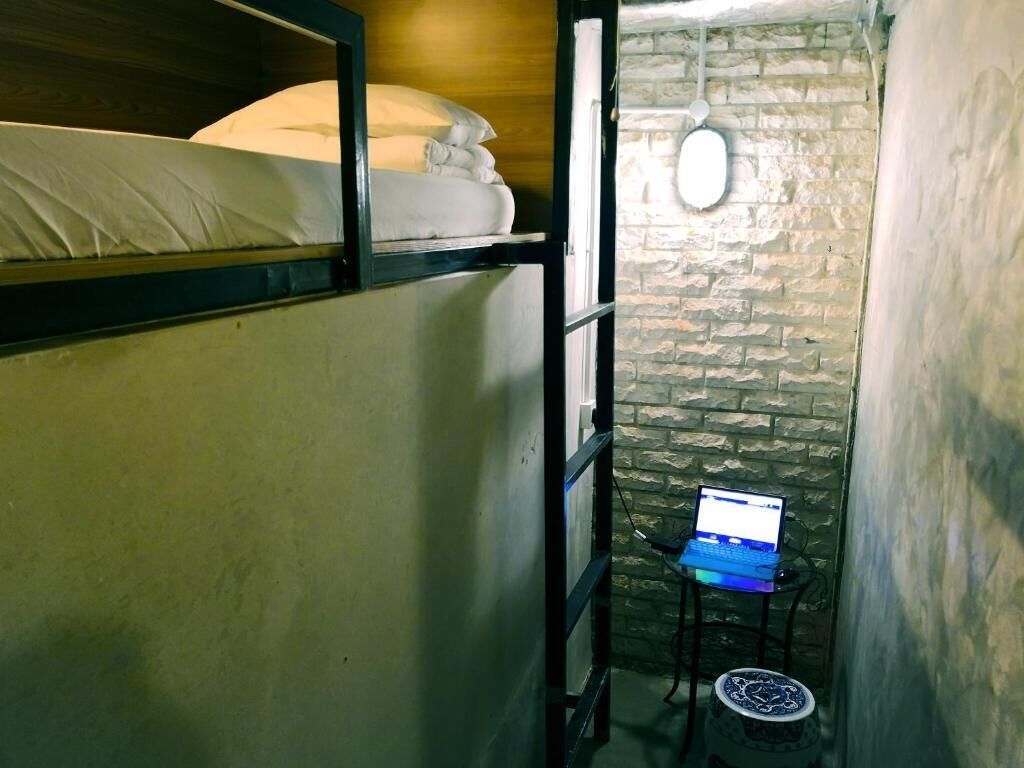 A small, rustic room with bunk beds, a laptop on a table, and a round table with a decorative item.
