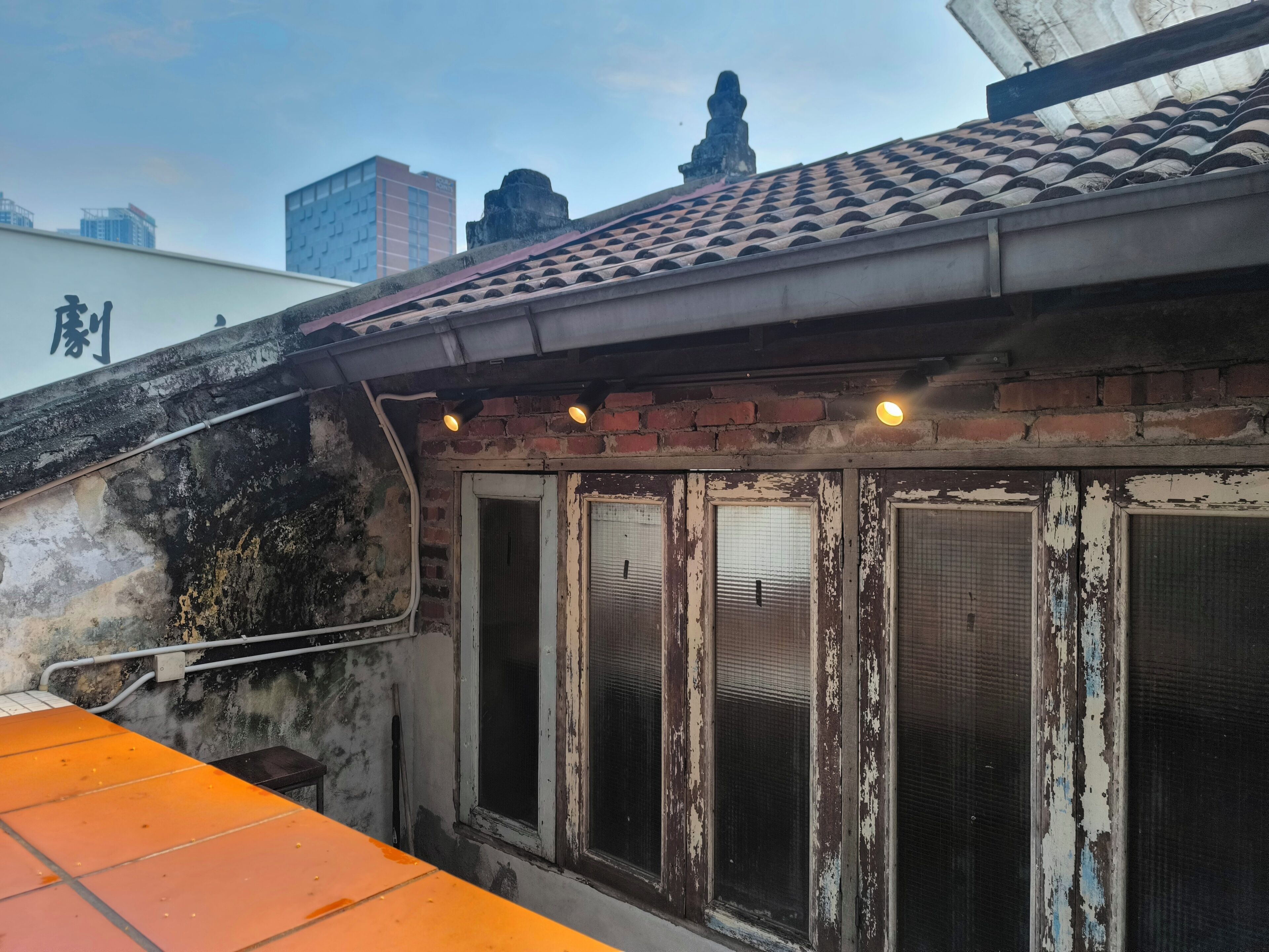 A rooftop with a tiled roof, a brick wall, and a metal railing.
