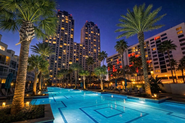 A hotel pool area with multiple pools, palm trees, and high-rise buildings in the background.