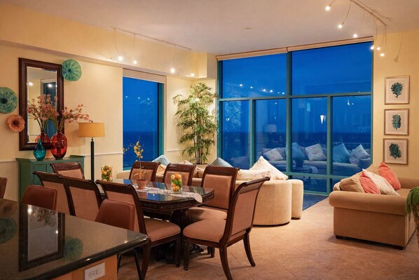 A dining area with a table and chairs, a large window with a view, and a sofa with cushions.