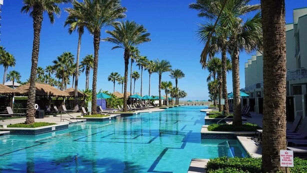 A pool area with lounge chairs and umbrellas, surrounded by palm trees. - Jr Penthouse 29th Floor Tallest Building SPI (South Padre Island)