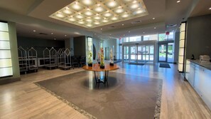 A spacious lobby with a central round table, a ceiling with recessed lighting, and a view through the glass doors.