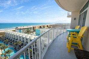 Un balcón con sillas amarillas, una piscina y vista a la playa y al océano.