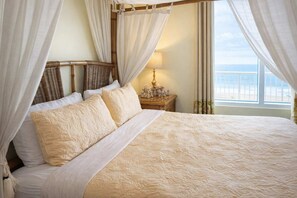 Una cama con dosel, una mesita de noche con lámpara y vistas al mar a través de una ventana.