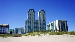 A beachfront hotel with two prominent high-rise buildings, a sandy beach, and palm trees.