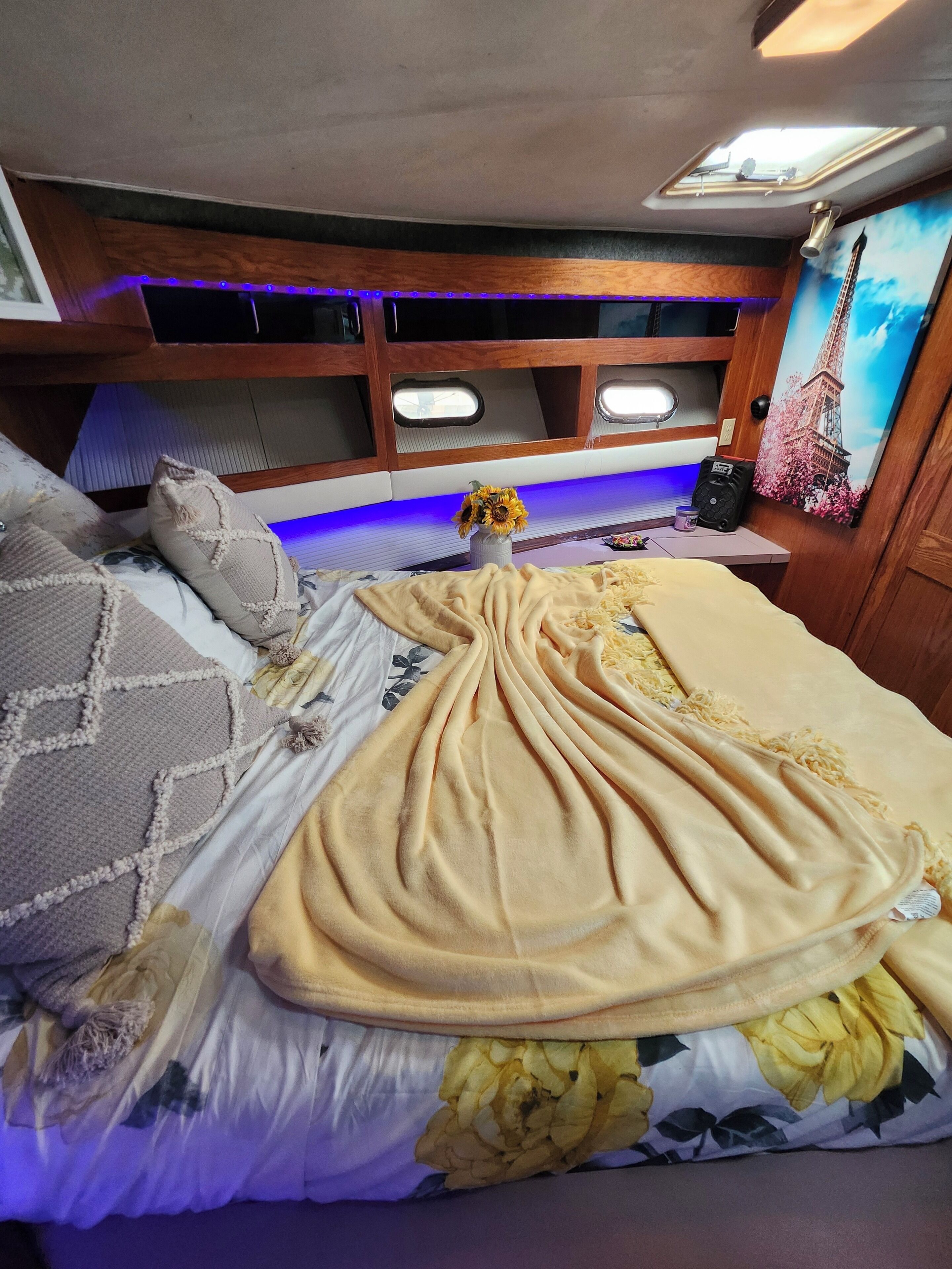 A bed with a floral bedspread, a beige blanket, and a vase with sunflowers.