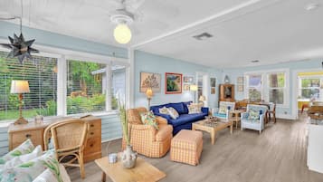 A spacious living room with a blue sofa, wicker furniture, and a dining area with a table and chairs.