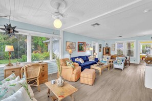 A spacious living room with a blue sofa, wicker furniture, and a dining area with a table and chairs. - Bromeliad Bungalow - Tropical Garden Retreat (Fort Lauderdale)